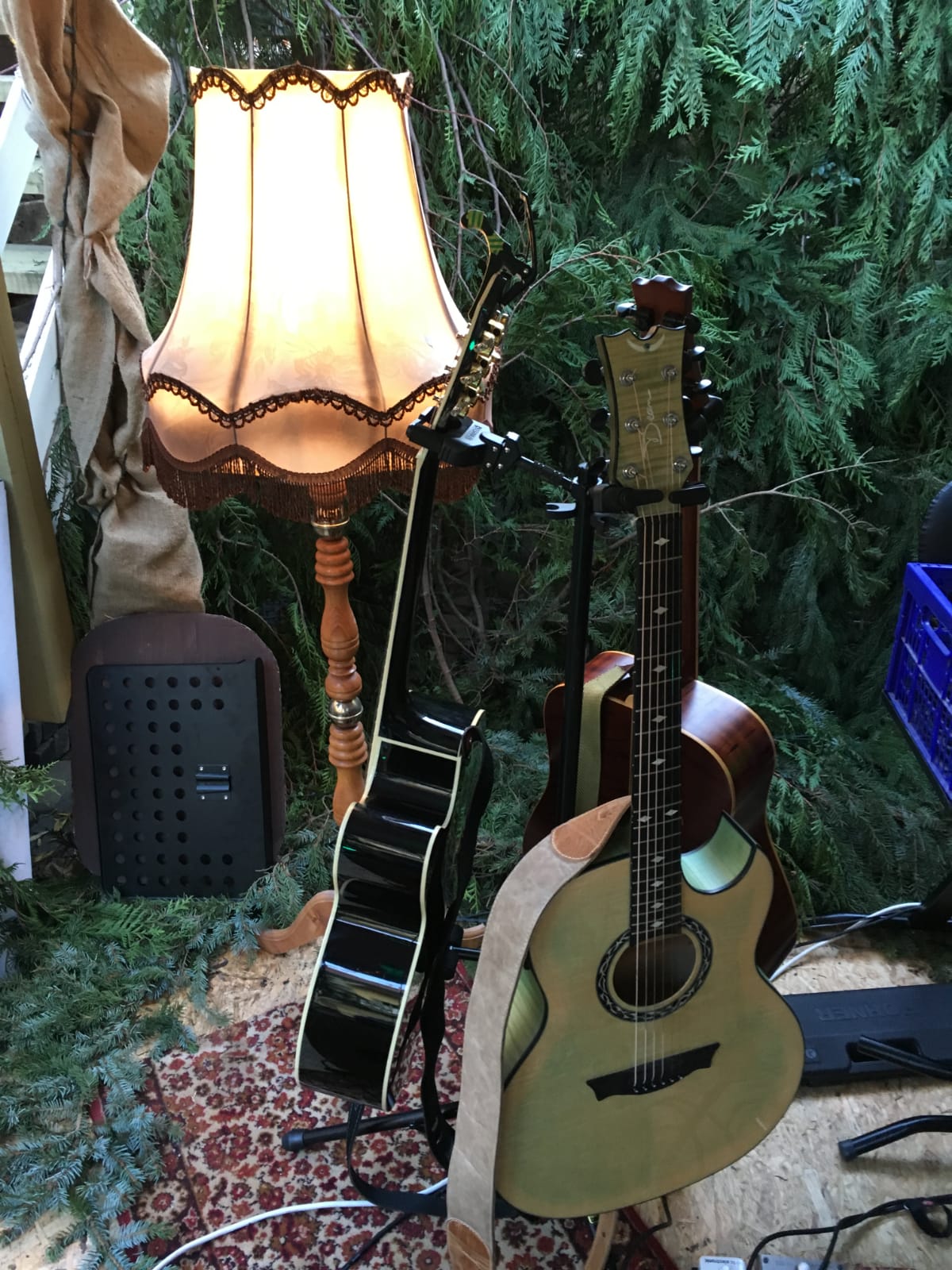 Auf dem Bild sieht man drei Gitarren am Gitarrenständer. Im Hintergrund steht eine Wohnzimmerlampe.